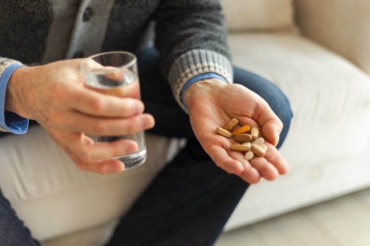 Man holding a range of different vitamins and a glass of water