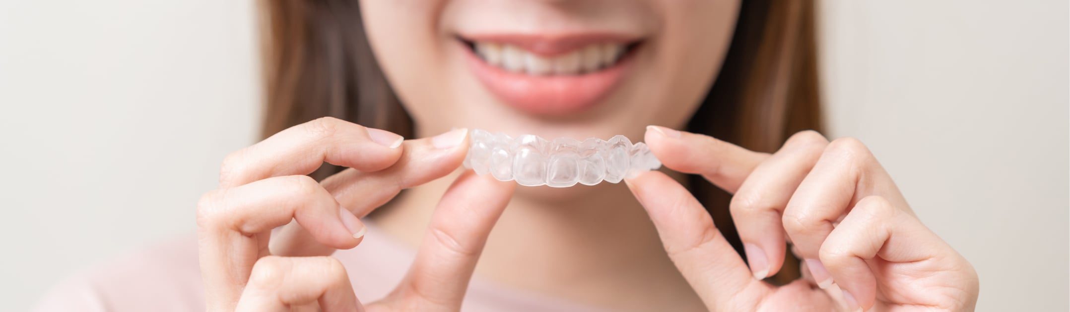 Woman holding a clear Invisalign aligner in front of her smile