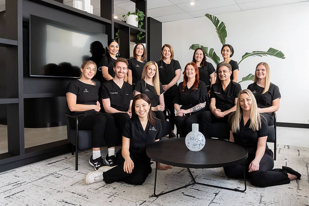 The 123 Dental team of thirteen in matching black scrubs, gathered in the practice's waiting lounge