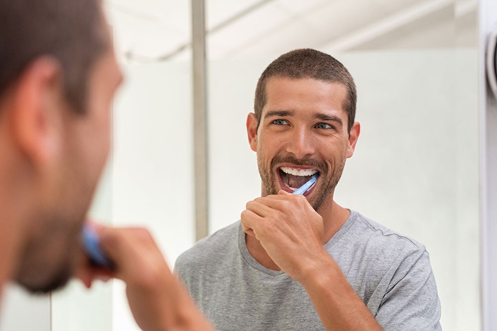 Man with veneers brushing teeth in mirror