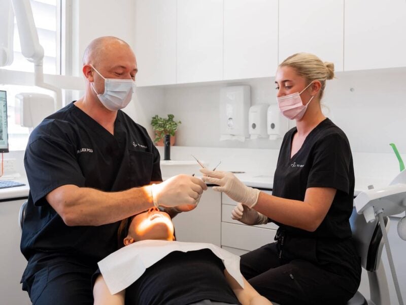 Dentist and assistant in black scrubs working on a reclined patient during a scale and clean
