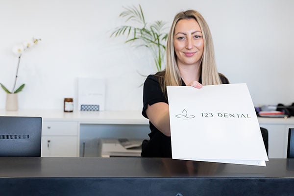 Receptionist holding a 123 Dental welcome sign at the front desk