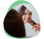 Patient smiling at her new straight teeth in a hand mirror held up in front of her