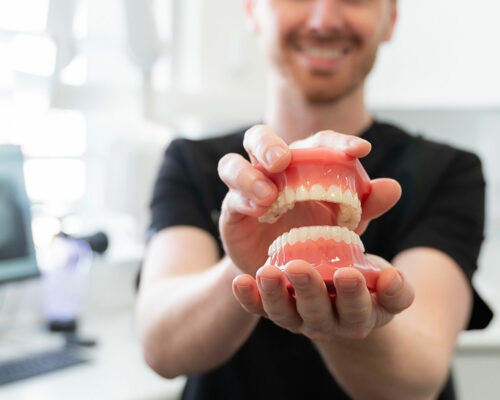Smiling team member in black scrubs holding out a full set of upper and lower dentures
