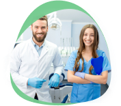 A dentist in a white coat and a colleague in blue scrubs smiling in a treatment room