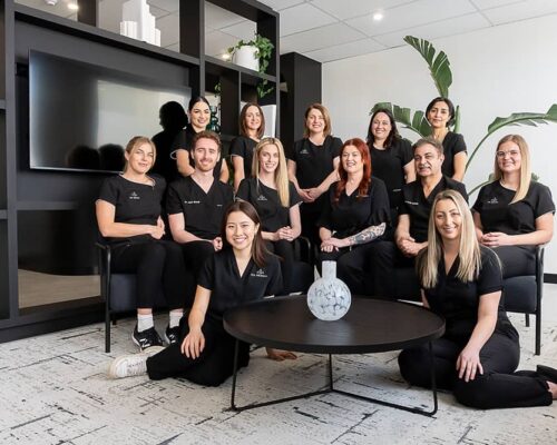 The 123 Dental team of fourteen in black scrubs gathered in the practice lounge
