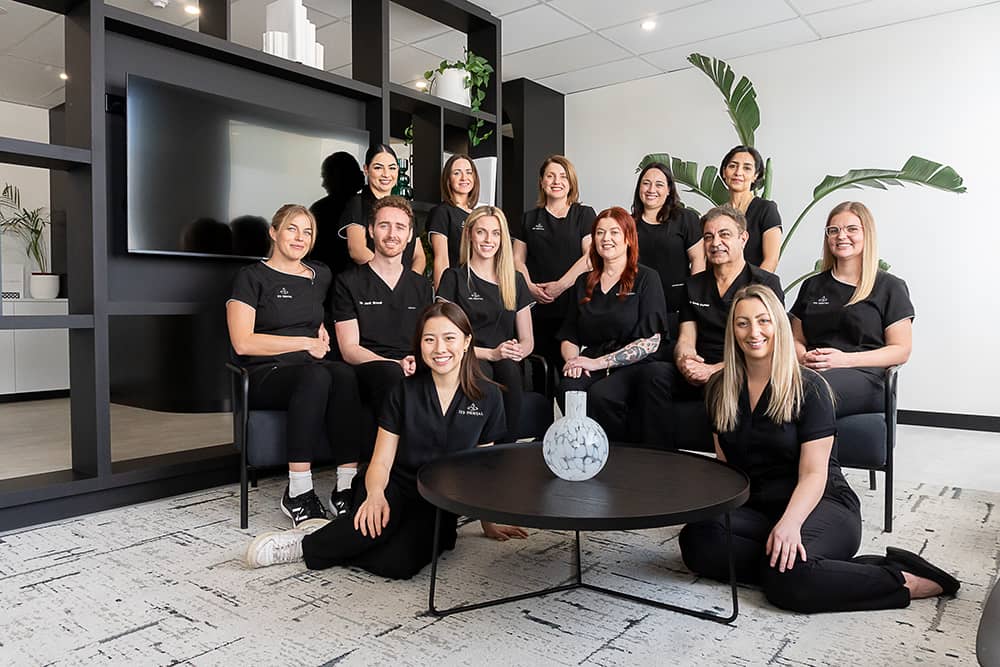 The 123 Dental team of thirteen in black scrubs gathered in the practice waiting area