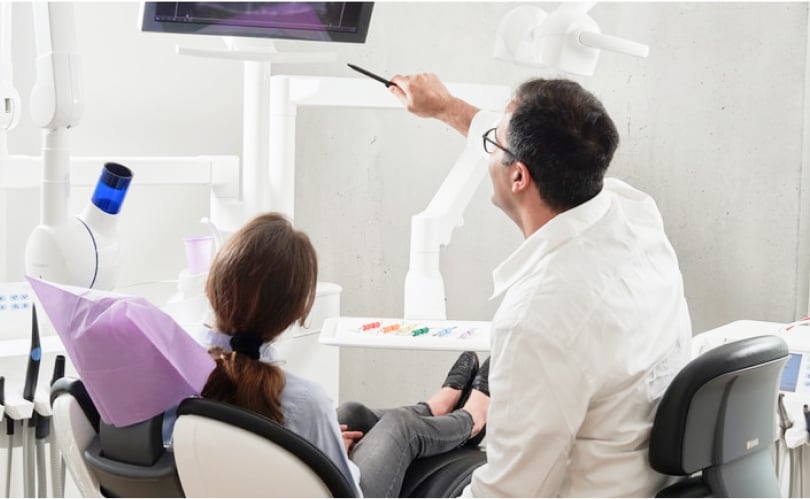 Dentist pointing at an X-ray on an overhead screen while a patient in the chair looks on