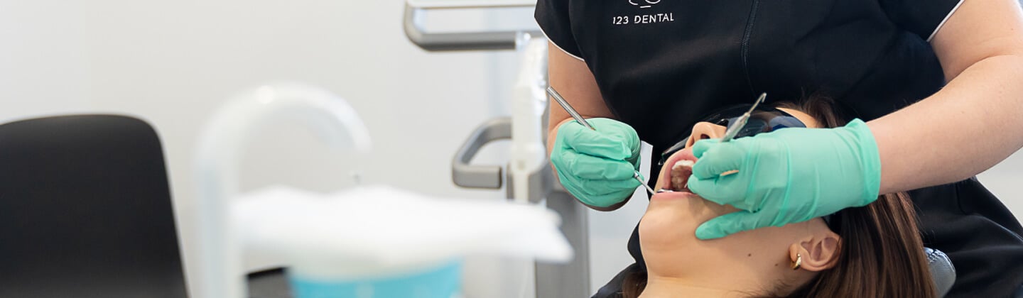 Dentist at 123 Dental examining a reclined patient's mouth with a mirror and probe