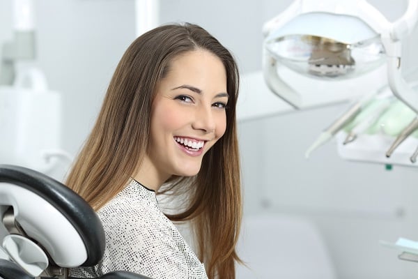 Smiling patient seated in a dental chair beside the overhead light and instrument tray